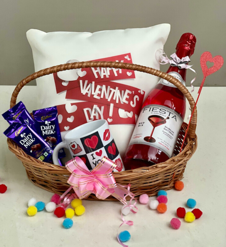 Valentine gift basket with Fiesta mocktail bottle, Dairy Milk chocolates, love theme mug and Happy Valentine’s Day cushion arranged in wicker basket