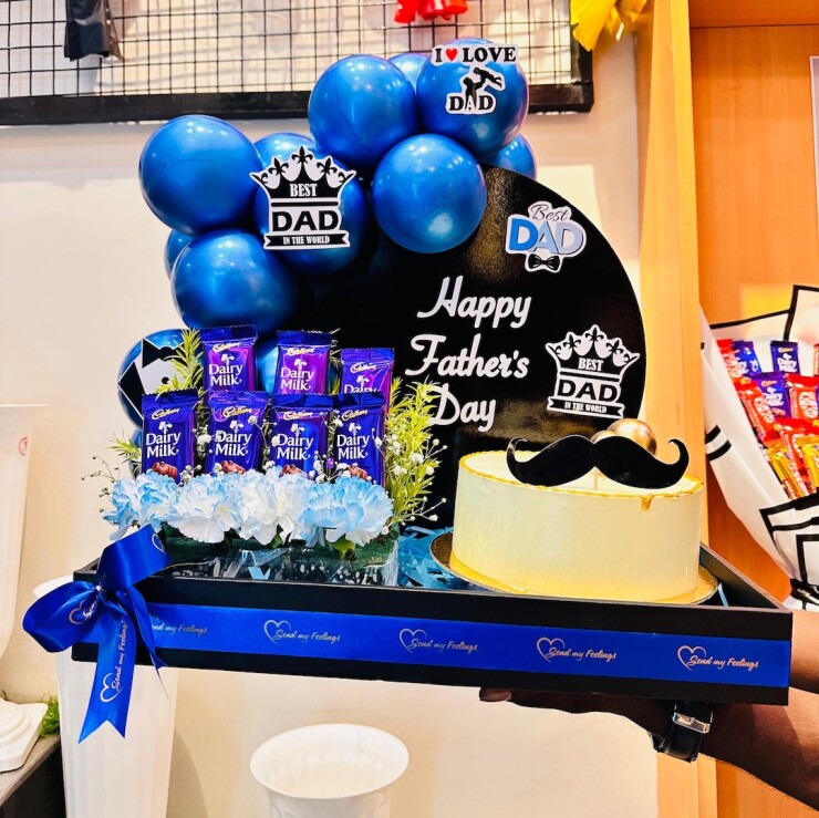 Super Dad Treat Hamper with 500 g fruit cake, Cadbury Dairy Milk chocolates, premium blue balloons, fresh flowers, and Father's Day decorations by Send My Feelings.