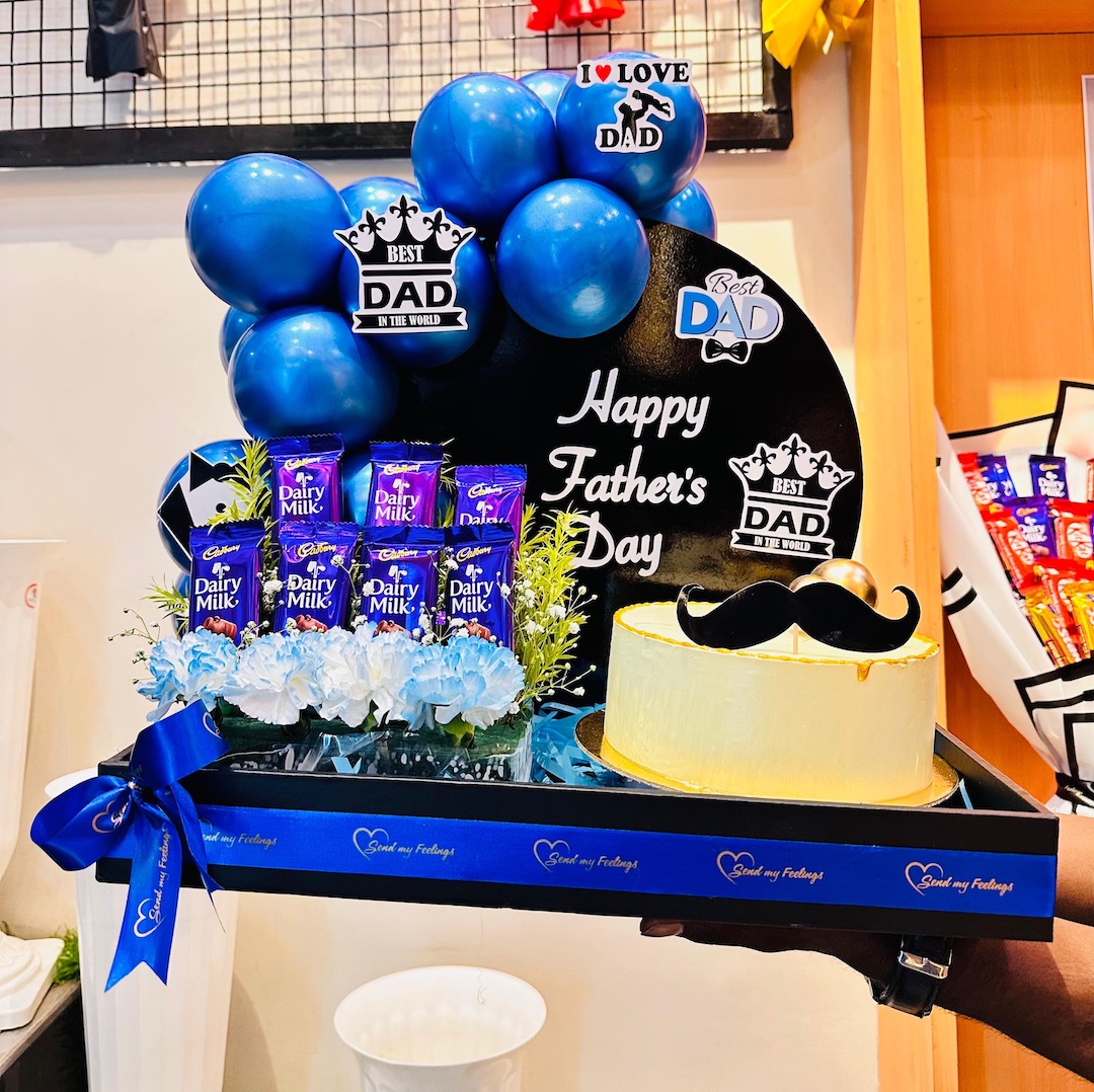 Super Dad Treat Hamper with 500 g fruit cake, Cadbury Dairy Milk chocolates, premium blue balloons, fresh flowers, and Father's Day decorations by Send My Feelings.